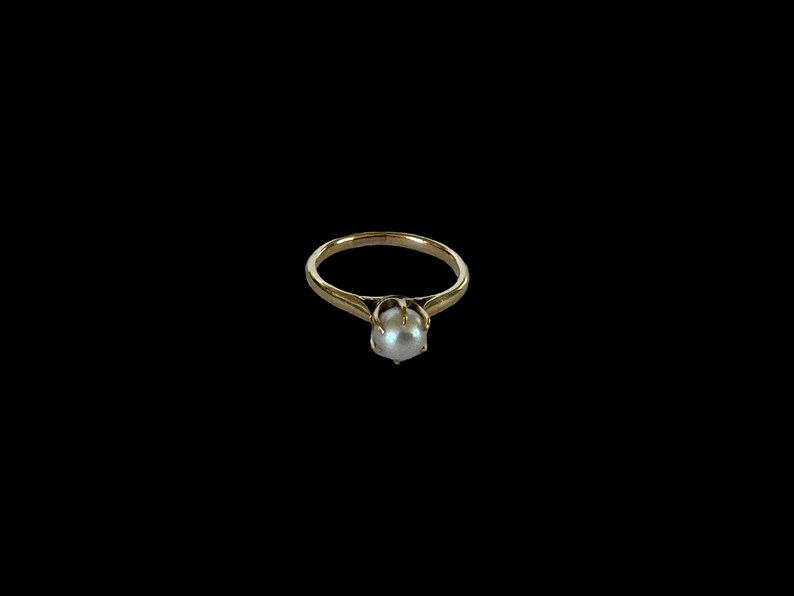 May include: A gold ring with a single white pearl set in the center.