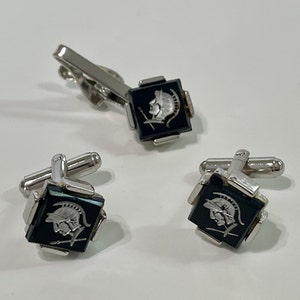 May include: A set of silver cufflinks and a tie clip with black square onyx stones featuring a silver etched design of a Roman soldier's head in profile.