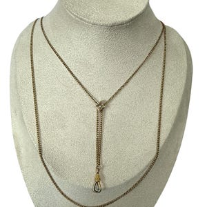 May include: A gold-toned lariat necklace featuring a delicate curb chain. The design includes a central square-shaped slider component with a small embedded stone, leading to a dangling drop section that terminates in a metal swivel clasp.