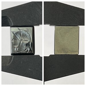 Op de afbeelding: Een zwarte en zilveren gegraveerde edelsteen met een profiel van een menselijk gezicht. De edelsteen wordt vastgehouden in een metalen klem.