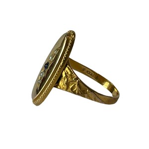 Peut inclure: Une bague en or avec un visage de forme ovale serti d'une pierre bleue et de perles blanches. La bande est grav&eacute;e d'un motif floral et du num&eacute;ro "700X".