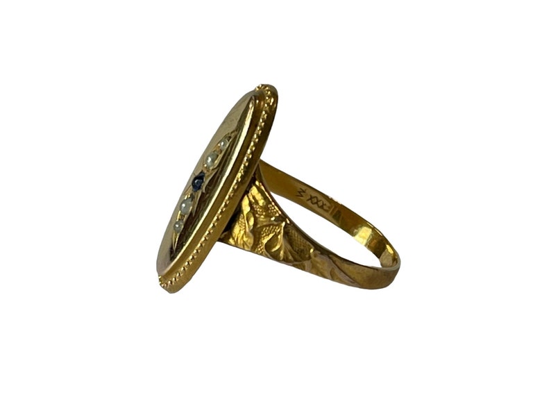Peut inclure: Une bague en or avec un visage de forme ovale serti d'une pierre bleue et de perles blanches. La bande est grav&eacute;e d'un motif floral et du num&eacute;ro "700X".