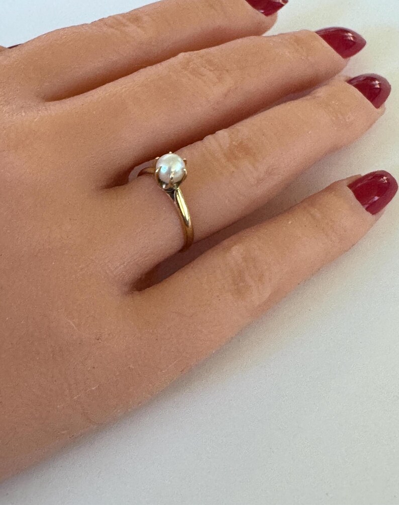 May include: A gold ring with a single white pearl set in a prong setting.