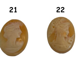 May include: Two oval-shaped cameo pendants with a white cameo image of a woman's profile on a yellow background. The cameo on the left is labeled "21" and the cameo on the right is labeled "22".