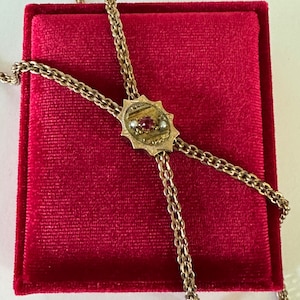 May include: A gold chain necklace with a red and white gemstone pendant. The necklace is displayed on a red velvet background.