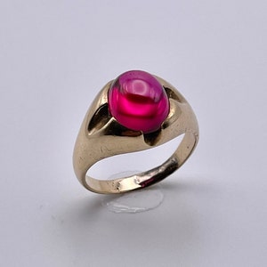 May include: A gold ring featuring a large, round, cabochon-cut, pink gemstone.