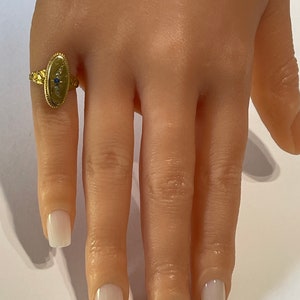 Peut inclure: Une bague en or avec un chaton ovale serti d'une pierre bleue et de petites pierres blanches. La bague est sur le doigt d'un mannequin.