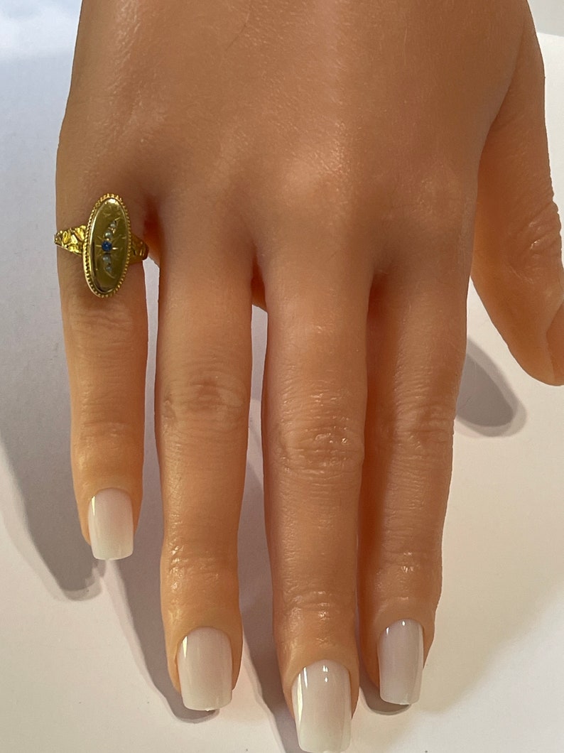 Peut inclure: Une bague en or avec un chaton ovale serti d'une pierre bleue et de petites pierres blanches. La bague est sur le doigt d'un mannequin.