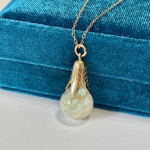 May include: A gold chain necklace with a pearlescent white opal pendant. The pendant is set in a gold setting with a leaf design.