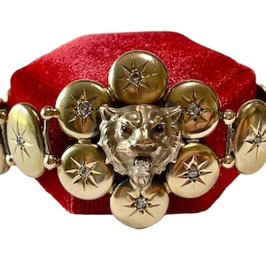 Peut inclure: Un bracelet en or avec un pendentif tête de tigre et des accents en forme d'étoile. Le bracelet est sur un coussin de velours rouge.
