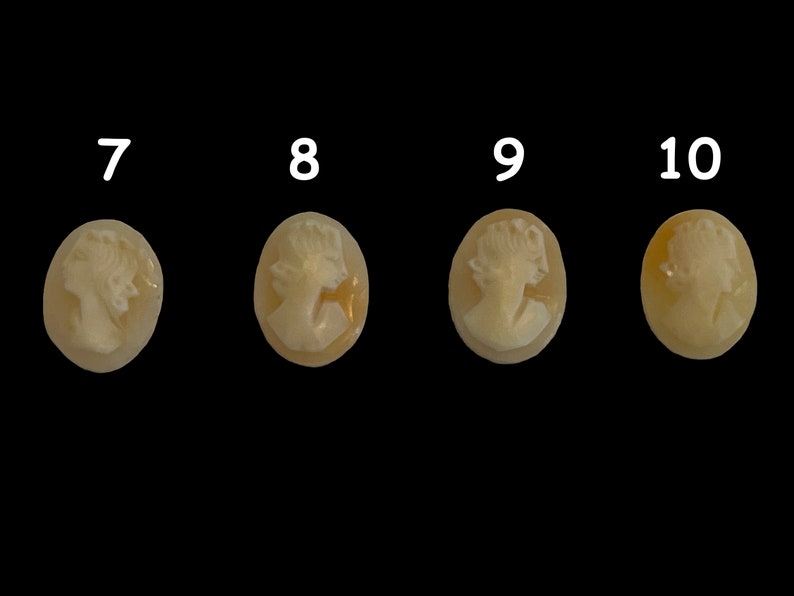 May include: Four oval-shaped cameo pendants with a white cameo image of a woman's profile on a light brown background.
