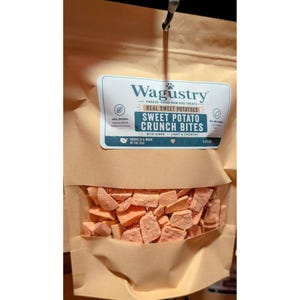 May include: A tan stand-up pouch of Wagustry freeze-dried dog treats labelled Real Sweet Potatoes Sweet Potato Crunch Bites. The bag features a clear window displaying orange, bite-sized, crunchy sweet potato pieces. Net weight is 73.7 grams.