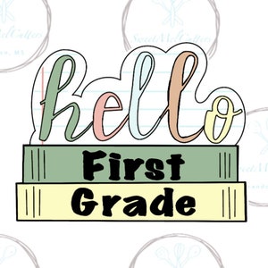 May include: A cookie cutter in the shape of a stack of books with the words "hello first grade" written on it. The books are green, yellow, and light blue. The words are in a colorful, handwritten font.