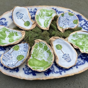 May include: Eight oyster shell dishes with gold trim and various green and blue floral patterns. The dishes are arranged on a white and blue patterned plate with gold trim.