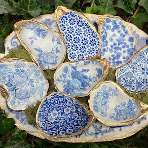 May include: Seven blue and white oyster shell dishes with gold trim. The dishes are arranged in a circle on a white surface with green moss.