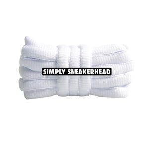 Peut inclure: Un ensemble de lacets blancs, soigneusement enroulés et attachés. Les lacets sont faits d'un matériau tissé. Le texte "SIMPLY SNEAKERHEAD" est affiché sur un rectangle noir.