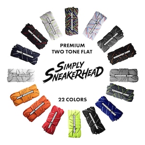 Op de afbeelding: Een verzameling van 22 paar premium tweekleurige platte veters in diverse kleuren, waaronder zwart, wit, blauw, oranje en rood. Elk paar is voorzien van het label "SIMPLY SNEAKERHEAD". De afbeelding staat op een witte achtergrond.