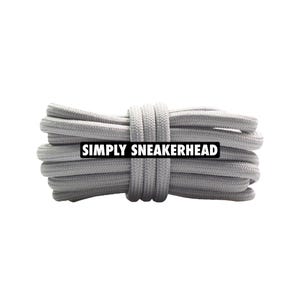 May include: A bundle of light gray shoelaces, tightly coiled and secured. The text "SIMPLY SNEAKERHEAD" is displayed on a black rectangle across the laces. The laces are made of a woven material.