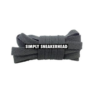 May include: A bundle of dark gray flat shoelaces, tightly coiled. The laces are made of a woven material. The text "SIMPLY SNEAKERHEAD" is displayed on a white rectangle across the laces.