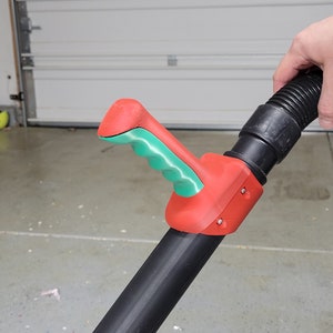 May include: A red and green plastic handle for a vacuum cleaner extension wand. The handle has a textured grip and is attached to a black extension wand.