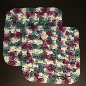 May include: Two crocheted dishcloths in a purple, teal, and white color pattern.