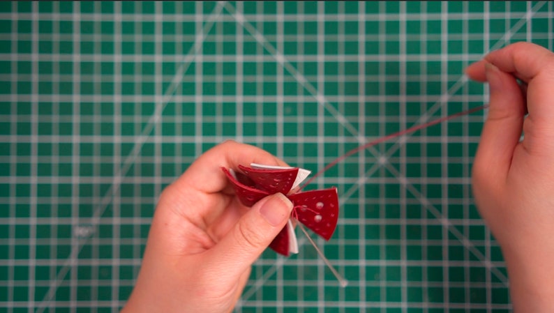 Peut inclure: Une fleur en papier rouge et blanche avec un cordon rouge attach&eacute;. La fleur est tenue par une main sur un tapis de coupe vert.