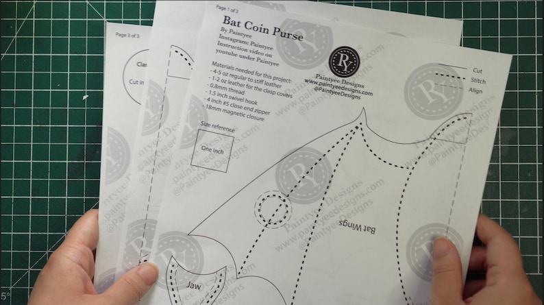 May include: Three white paper sheets with printed instructions and patterns for a bat-shaped coin purse. The sheets include text, dotted lines, and a size reference of one inch. The sheets are held over a green grid.