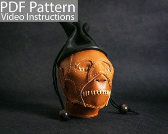 May include: A brown leather mask with stitched details, resembling a human face. The mask is attached to a black leather hat with a long cord.