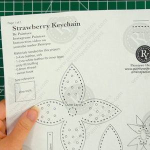 May include: A black and white printable pattern for a strawberry keychain. The pattern includes instructions for cutting, stitching, and aligning the pieces. The pattern also includes a size reference of one inch.