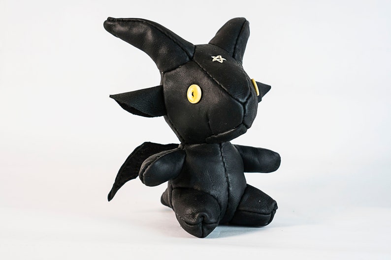 May include: Black leather stuffed toy shaped like a goat with yellow eyes and a star on its forehead.