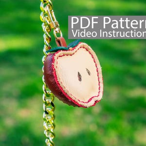 Op de afbeelding: Een rode en witte leren appel sleutelhanger met een gouden ketting. De sleutelhanger heeft een PDF-patroon en video-instructies.