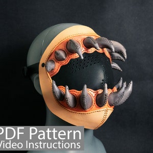 Puede incluir: Una máscara de cuero con una boca negra y garras naranjas. La máscara está en una cabeza de maniquí gris. El texto "PDF Pattern Video Instructions" está en la parte inferior de la imagen.