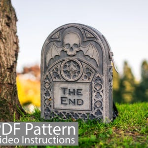 Może przedstawiać: Szary skórzany plecak w kształcie nagrobka z motywem czaszki i skrzydeł nietoperza. Plecak ma napis "The End".