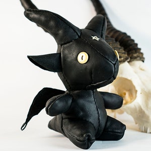 May include: A black leather toy dragon with wings, horns, and button eyes. The dragon is sitting next to a white animal skull.