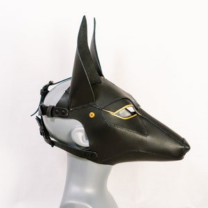 May include: Black leather Anubis mask with gold accents and a blue strap. The mask has a long snout and pointed ears.