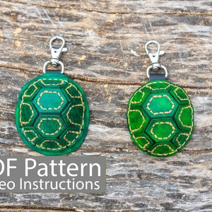May include: Two green leather turtle keyrings with gold stitching on a wooden background. The text "PDF Pattern Video Instructions" is at the bottom of the image.