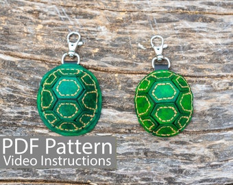 Peut inclure: Deux porte-clés en cuir vert en forme de tortue avec des coutures dorées sur un fond en bois. Le texte "PDF Pattern Video Instructions" est en bas de l'image.
