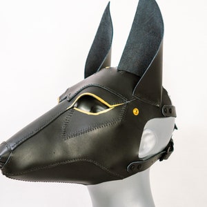 May include: Black leather mask with gold accents and pointed ears. The mask is designed to resemble an animal head, possibly a dog or wolf.