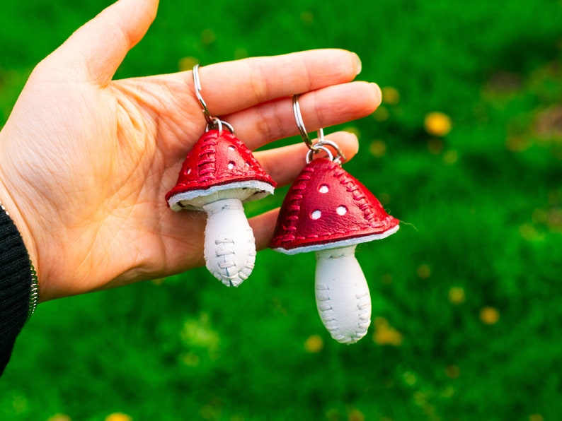 Peut inclure: Deux porte-cl&eacute;s en forme de champignon en cuir rouge et blanc avec des coutures blanches et des points blancs sur les chapeaux rouges.