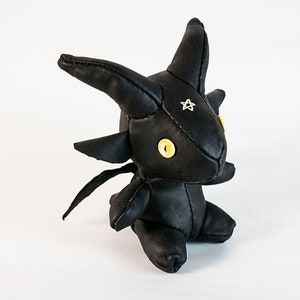 May include: A black leather plush toy shaped like a dragon with yellow button eyes and a silver star on its forehead.