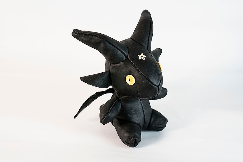 May include: A black leather plush toy shaped like a dragon with yellow button eyes and a silver star on its forehead.