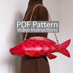 May include: A red fish-shaped handbag with a gold chain strap. The bag is made of leather and features detailed stitching and a fin design. The text "PDF Pattern Video Instructions" is displayed on the image.