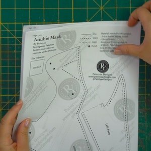 May include: A black and white Anubis mask pattern with the text "Anubis Mask" and "Paintree Designs" printed on it. The pattern is on a white sheet of paper.