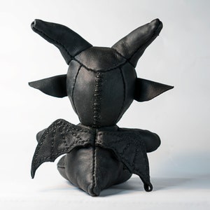 May include: Black leather toy with horns and wings. The toy is sitting on a white surface.