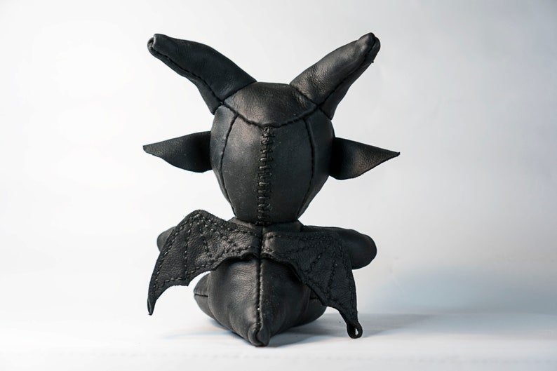 May include: Black leather toy with horns and wings. The toy is sitting on a white surface.
