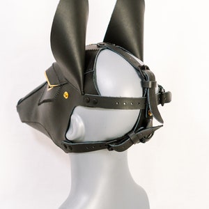 May include: Black leather mask with gold accents and adjustable straps. The mask has two large ears and a snout.