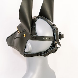 May include: Black leather mask with gold accents and adjustable straps. The mask has two large ears and a snout.