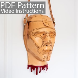 May include: A tan leather crossbody bag shaped like a stylized human head with black stitched details. The bag has a red, dripping blood-like design at the bottom. The text "PDF Pattern Video Instructions" is at the top.