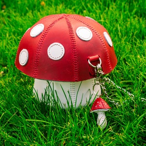 Peut inclure: Un sac &agrave; main en cuir rouge et blanc en forme de champignon, avec une bandouli&egrave;re en cuir blanc et un petit charme en forme de champignon rouge et blanc attach&eacute; &agrave; une cha&icirc;ne argent&eacute;e.