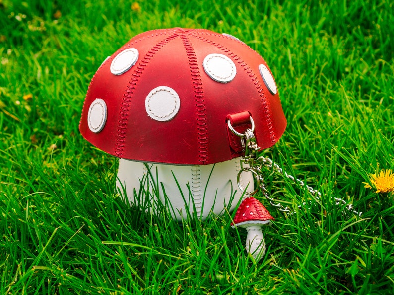 Peut inclure: Un sac &agrave; main en cuir rouge et blanc en forme de champignon, avec une bandouli&egrave;re en cuir blanc et un petit charme en forme de champignon rouge et blanc attach&eacute; &agrave; une cha&icirc;ne argent&eacute;e.